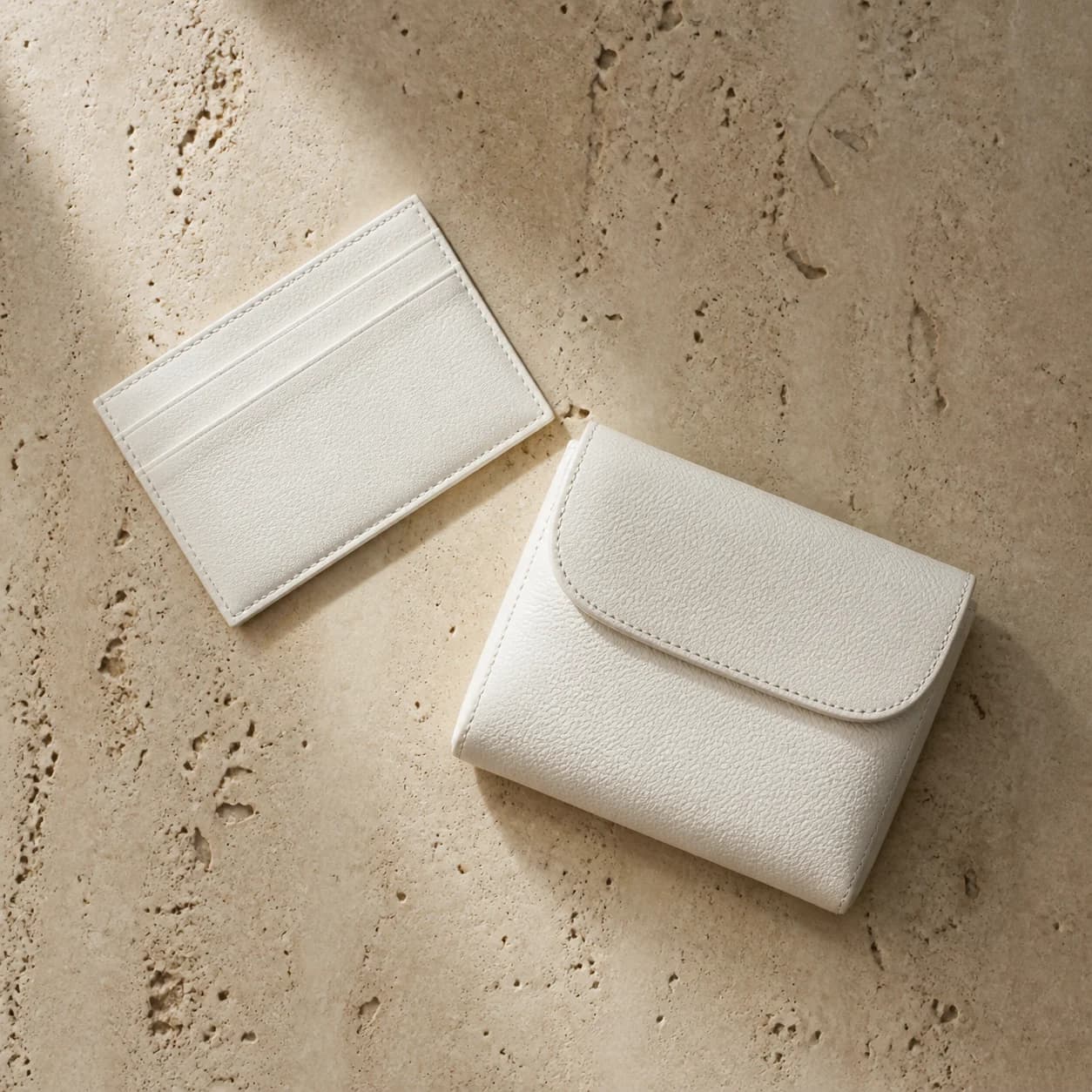 Chalk leather cardholder and mini purse arranged on raw travertine